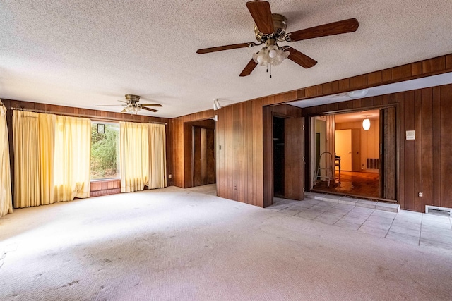 carpeted empty room with ceiling fan, a textured ceiling, and wooden walls