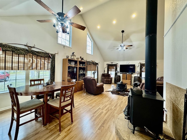 dining room featuring high vaulted ceiling, a wood stove, ceiling fan, and light hardwood / wood-style flooring