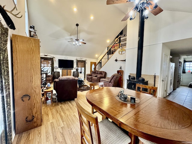 dining area with ceiling fan, high vaulted ceiling, a wood stove, and light wood-type flooring