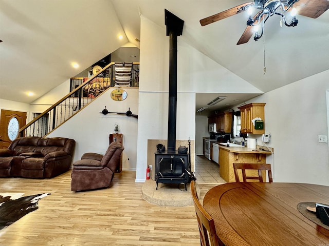 living room featuring lofted ceiling, a wood stove, ceiling fan, and light hardwood / wood-style flooring