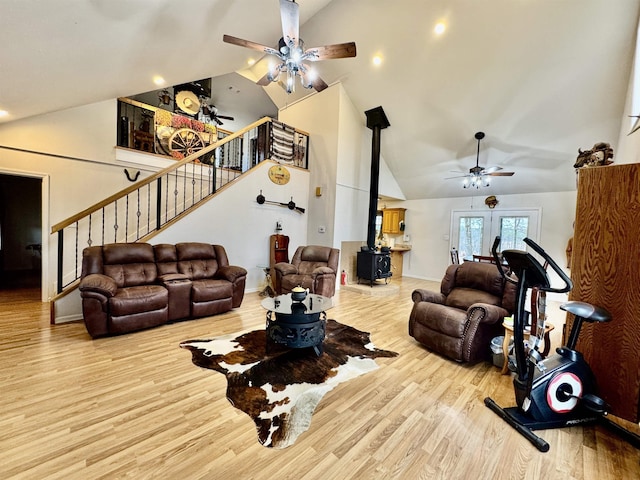 living room with ceiling fan, high vaulted ceiling, a wood stove, and light hardwood / wood-style floors