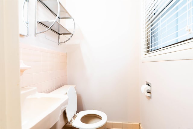 bathroom with a sink, toilet, and tile walls