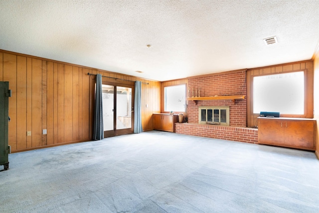 unfurnished living room with visible vents, carpet flooring, a textured ceiling, and wood walls
