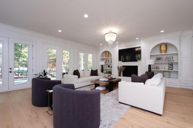 living room featuring built in shelves, ornamental molding, plenty of natural light, and light wood-type flooring