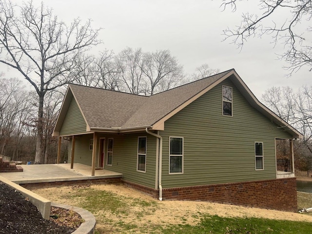 view of side of property with a shingled roof, crawl space, and a patio area