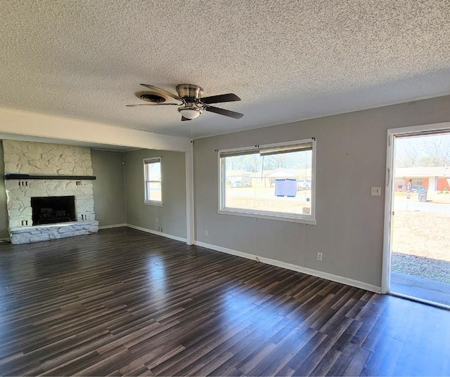 unfurnished living room with ceiling fan, a stone fireplace, a textured ceiling, and dark hardwood / wood-style flooring