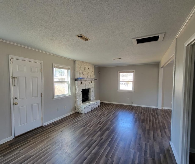 unfurnished living room with ornamental molding, a stone fireplace, dark hardwood / wood-style floors, and a textured ceiling