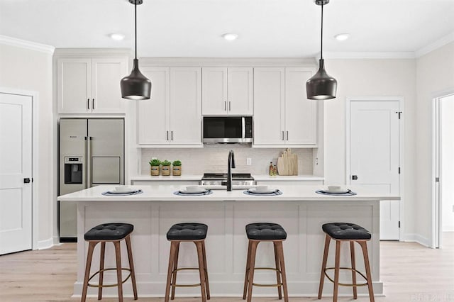 kitchen featuring appliances with stainless steel finishes, white cabinets, hanging light fixtures, a kitchen island with sink, and crown molding