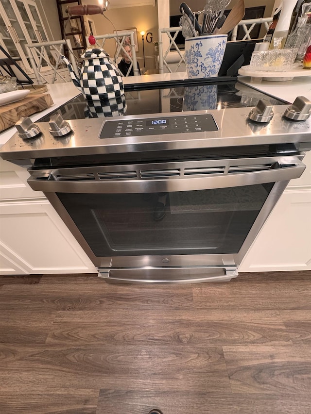 interior details with dark wood-type flooring, white cabinets, and electric range