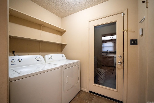 clothes washing area with sink, a textured ceiling, washing machine and clothes dryer, and dark tile patterned flooring