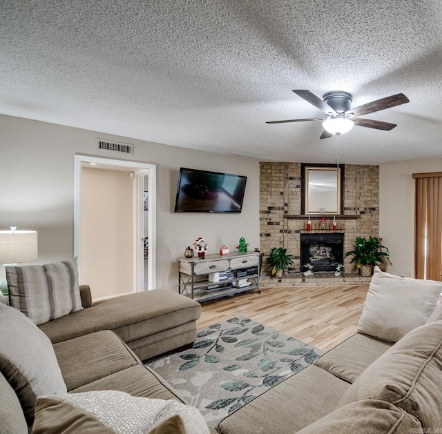 living room featuring ceiling fan, hardwood / wood-style floors, a textured ceiling, and a fireplace