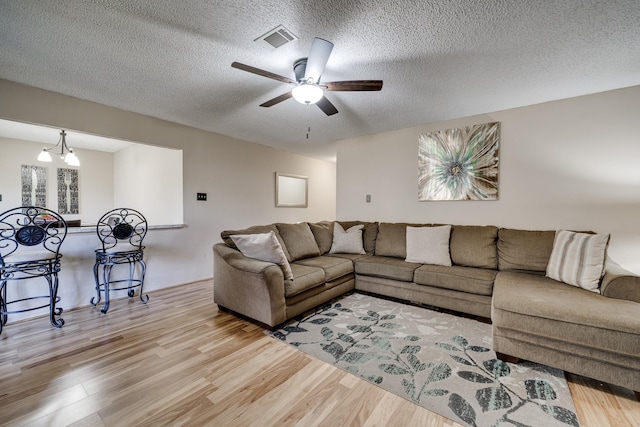 living room featuring ceiling fan with notable chandelier, light hardwood / wood-style flooring, and a textured ceiling