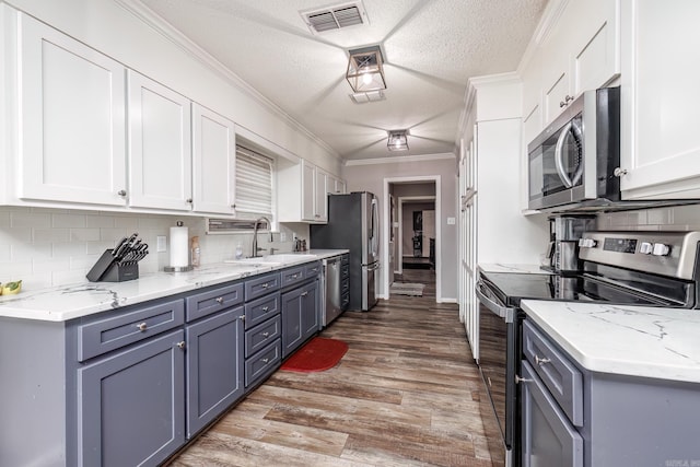 kitchen with white cabinetry, ornamental molding, appliances with stainless steel finishes, and sink