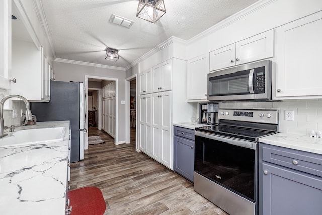 kitchen with white cabinetry, sink, ornamental molding, stainless steel appliances, and light hardwood / wood-style flooring