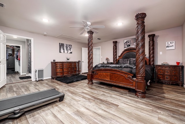 bedroom featuring decorative columns, a walk in closet, radiator heating unit, ceiling fan, and hardwood / wood-style floors