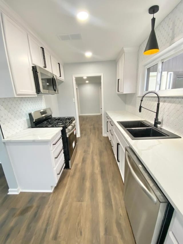 kitchen featuring sink, white cabinetry, hanging light fixtures, appliances with stainless steel finishes, and light stone countertops