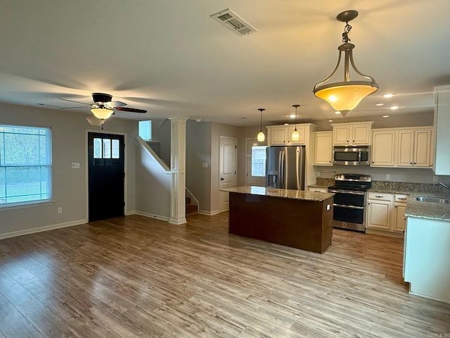 kitchen with sink, a kitchen island, pendant lighting, stainless steel appliances, and white cabinets