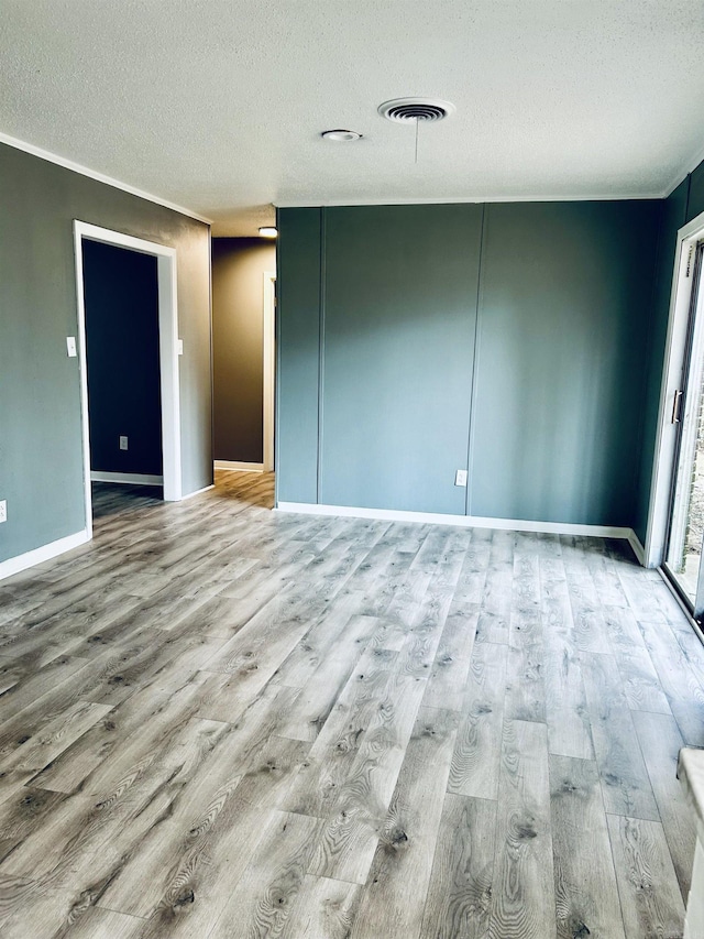 spare room with ornamental molding, a textured ceiling, and light wood-type flooring