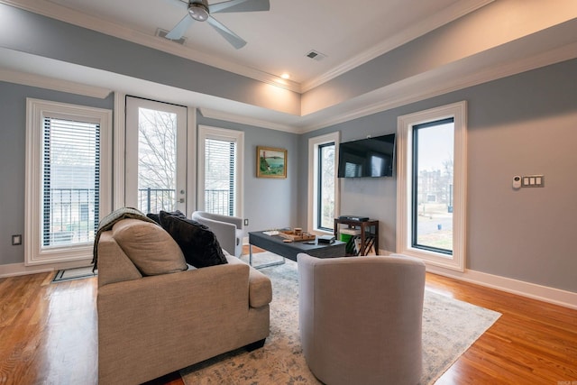 living room with crown molding, ceiling fan, light hardwood / wood-style floors, and a tray ceiling