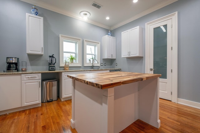 kitchen with crown molding, wooden counters, a center island, light hardwood / wood-style floors, and white cabinets