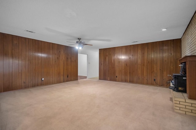 unfurnished living room with ceiling fan, light colored carpet, and wood walls