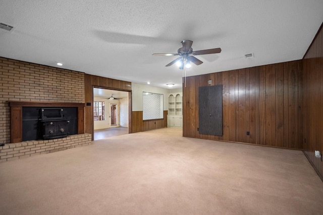 unfurnished living room with light colored carpet, a textured ceiling, ceiling fan, and wood walls