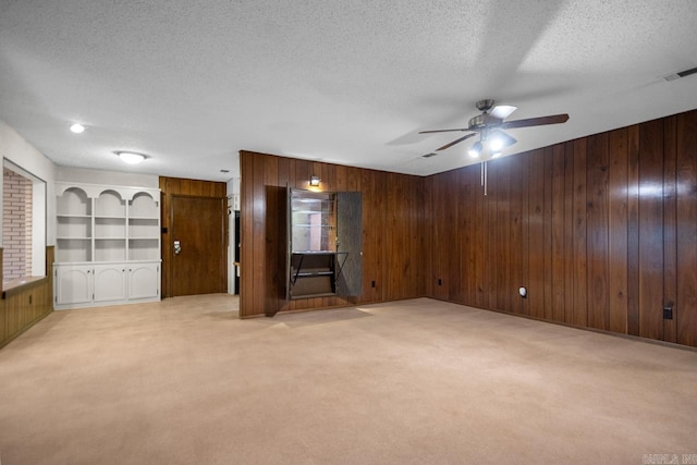 unfurnished living room with light carpet, ceiling fan, wooden walls, and a textured ceiling