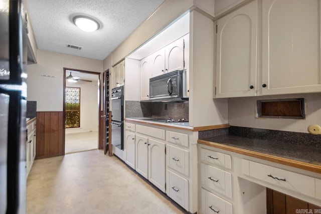 kitchen with white cabinetry, wooden walls, tasteful backsplash, black appliances, and a textured ceiling