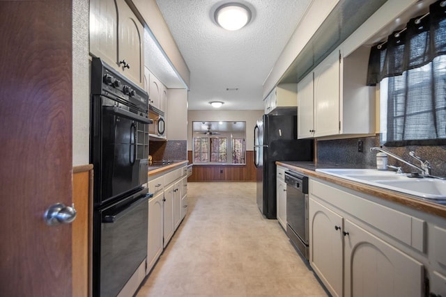 kitchen with sink, wooden walls, black appliances, a textured ceiling, and white cabinets