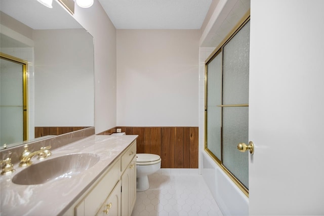 full bathroom with wood walls, shower / bath combination with glass door, tile patterned flooring, vanity, and toilet