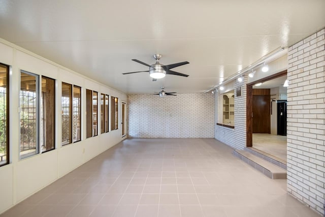 tiled empty room with brick wall, track lighting, and ceiling fan