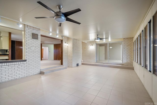 empty room featuring light tile patterned flooring, brick wall, and ceiling fan