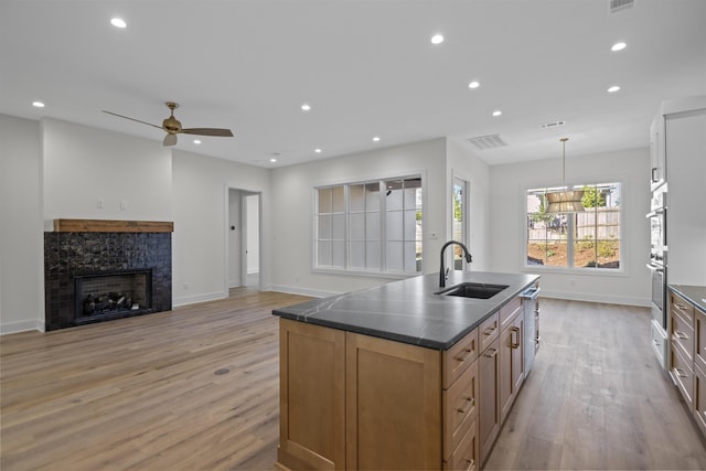 kitchen featuring a sink, hanging light fixtures, brown cabinets, dark countertops, and a center island with sink