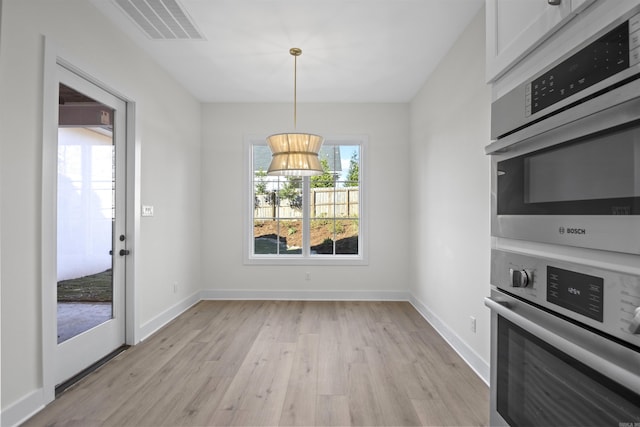 unfurnished dining area featuring light wood finished floors, plenty of natural light, visible vents, and baseboards