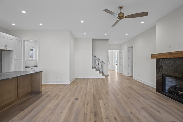 unfurnished living room featuring light wood-style floors, stairs, a tiled fireplace, and recessed lighting