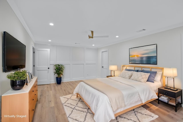 bedroom featuring ornamental molding, light wood-style flooring, visible vents, and a decorative wall