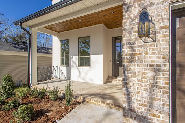 doorway to property with stucco siding, a porch, and brick siding