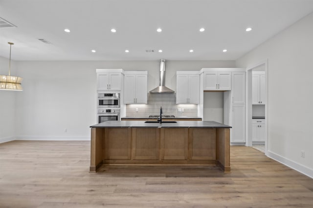 kitchen with visible vents, an island with sink, appliances with stainless steel finishes, wall chimney range hood, and white cabinetry