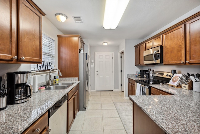 kitchen featuring light stone counters, stainless steel appliances, sink, and light tile patterned floors