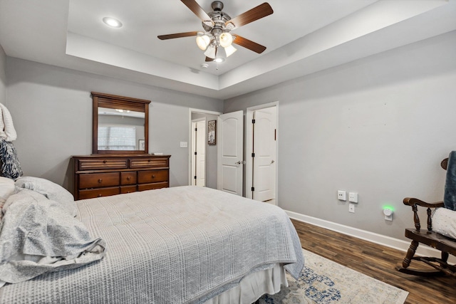 bedroom with dark wood-type flooring, ceiling fan, and a tray ceiling