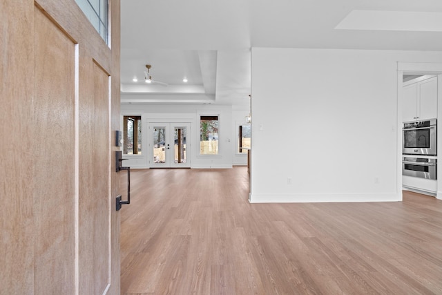 interior space featuring french doors, a tray ceiling, and light wood-type flooring