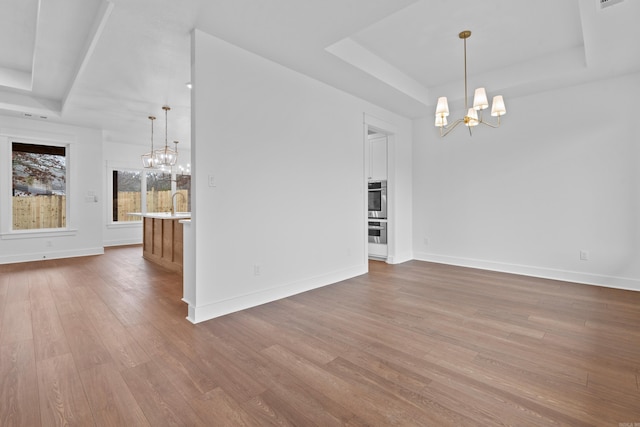 unfurnished living room with a raised ceiling, sink, an inviting chandelier, and light hardwood / wood-style flooring