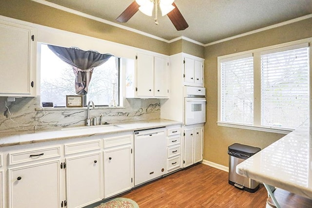 kitchen with sink, crown molding, white appliances, wood-type flooring, and white cabinets