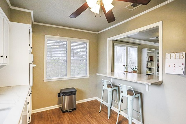 kitchen with hardwood / wood-style flooring, crown molding, a breakfast bar, and white cabinets