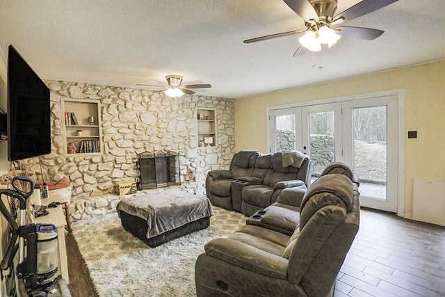 living room featuring french doors, a stone fireplace, a textured ceiling, ceiling fan, and hardwood / wood-style floors