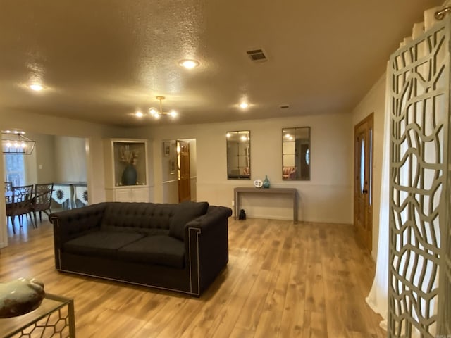 living room with a textured ceiling, a chandelier, and light hardwood / wood-style flooring