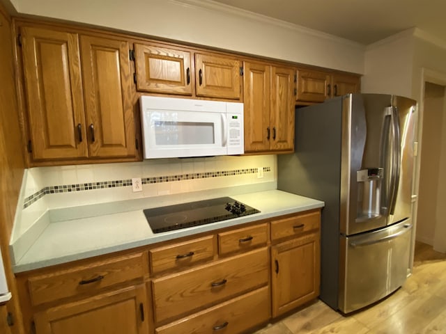 kitchen with crown molding, black electric stovetop, stainless steel fridge, and decorative backsplash