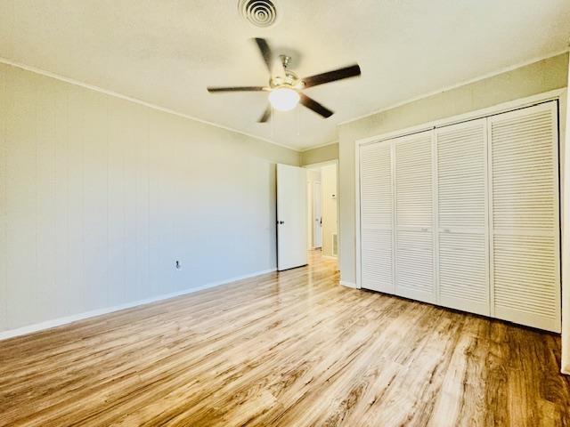 unfurnished bedroom with crown molding, light hardwood / wood-style floors, a closet, and ceiling fan