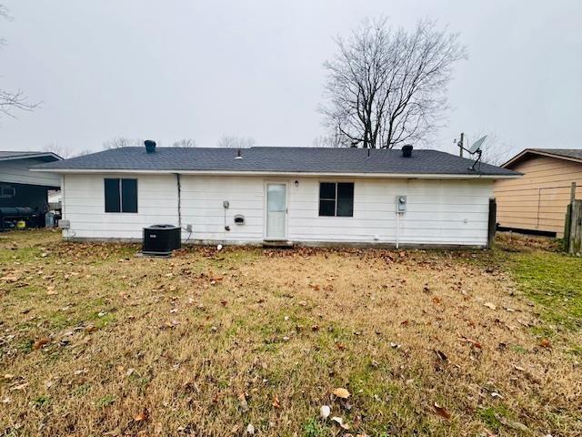 rear view of house featuring central AC unit and a lawn