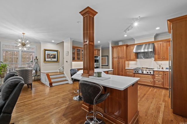 kitchen featuring wall chimney range hood, hanging light fixtures, stainless steel appliances, a kitchen breakfast bar, and light wood-type flooring